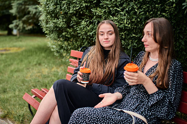 istock Young girlfriends gossiping on park bench with coffee in casual afternoon setting 2248401585