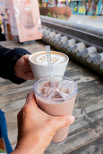 Hands holding refreshing iced chocolate drink and hot latte, friends toasting outside a cafe