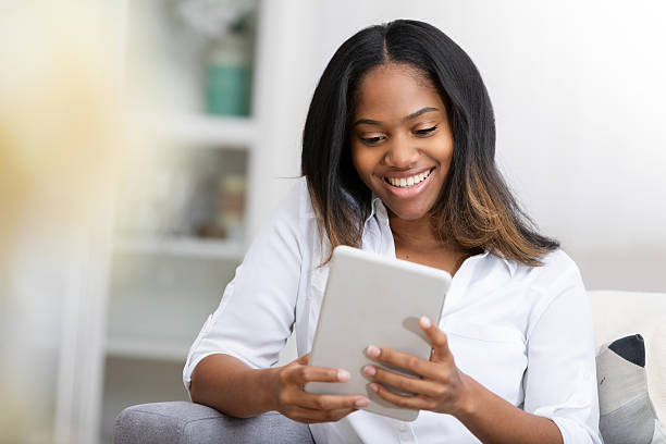 istock Young Black woman happily smiles while looking at a digital tablet indoors. 2248404991