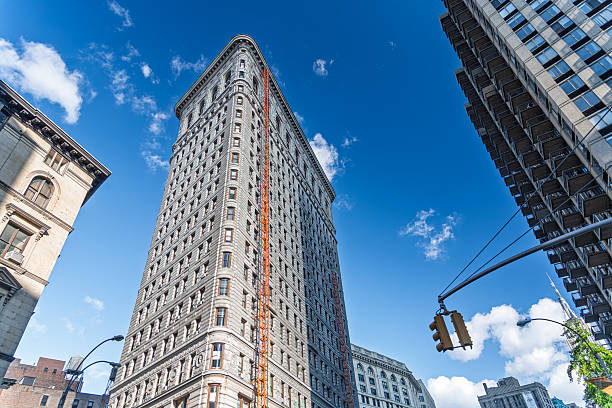 The Flatiron Building stands tall in Midtown Manhattan, showcasing its unique architecture under a bright blue sky on a sunny day.