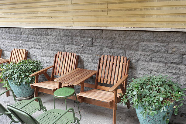 Wooden chairs and a small table sit beside potted plants against a wall.
