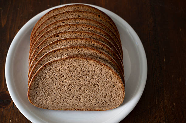 Close-up of freshly sliced whole grain bread arranged on a wooden board and cooling rack. Rustic homemade loaf with natural texture, ideal for concepts of healthy eating, bakery products, organic food, breakfast, and traditional baking.