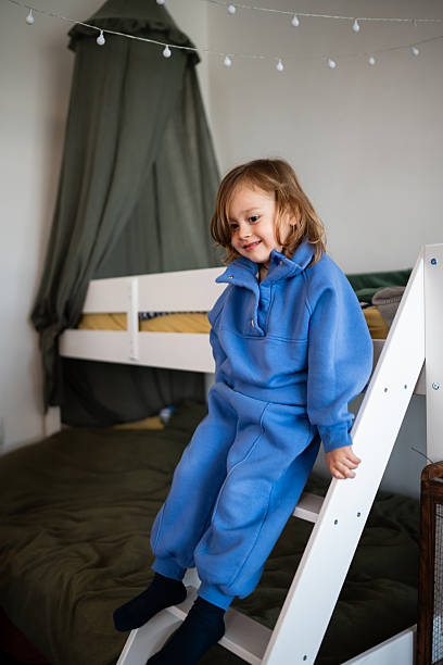 istock Happy child in blue pajamas climbing bunk bed ladder 2248412199