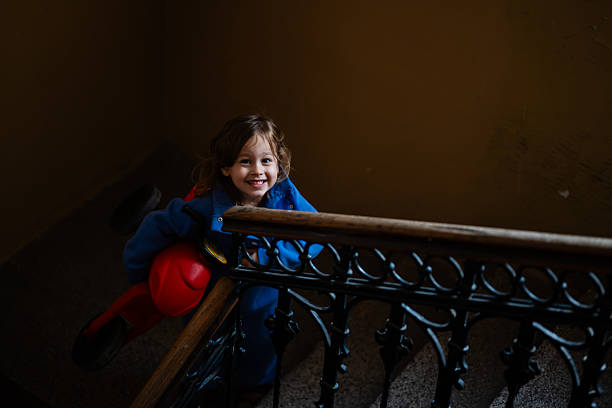 Young boy playing with a red toy motorcycle on an indoor staircase, looking at the camera and smiling with joy