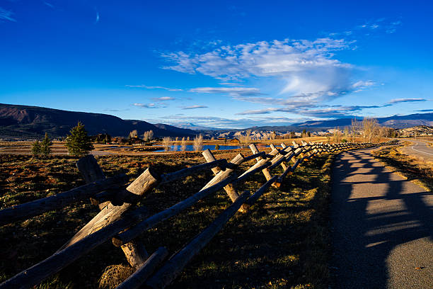 Scenic rural mountain area with wood fence running along recreation path casting long shadows on path with distant mountain views during golden hour.