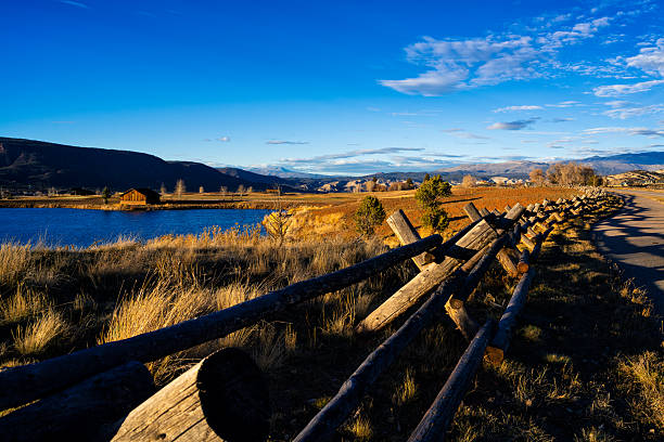 Scenic rural mountain area with wood fence running along recreation path casting long shadows on path with distant mountain views during golden hour.