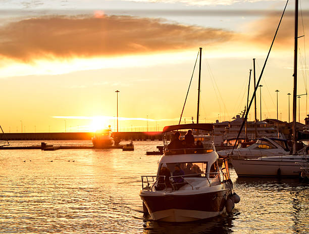 SOCHI, RUSSIA – JANUARY 3, 2018: A motorboat with passengers returns to the marina during a bright winter sunset at the Sochi seaport. Several yachts and sailboats are moored nearby, with warm evening light reflecting on the water. The scene captures everyday leisure activity at the port during the holiday season. Editorial use only.