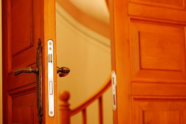 A wooden door swings open, exposing a well-lit curved staircase.