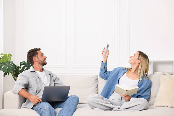 istock Couple with laptop and book using remote to control air conditioner on sofa at home 2248422792