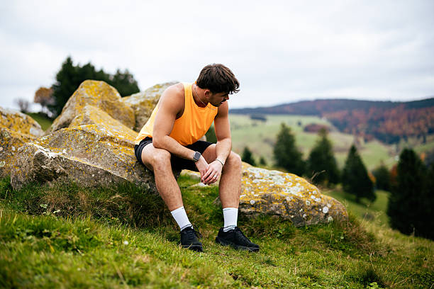 Trail runner pauses on rock in meadow on autumn day
