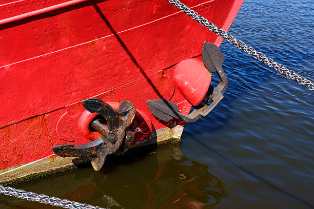 A red boat with a black anchor on it. The anchor is rusty and the boat is in the water