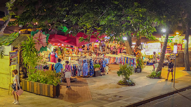 Waikiki, Hawaii, February 24, 2018:  A vibrant street market comes alive under the canopy of lush trees in Waikiki, offering colorful clothing and local souvenirs to evening shoppers enjoying Hawaii's warm tropical ambiance