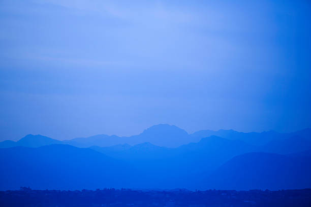 A serene blue mountain landscape shows multiple distant ridges fading into the horizon, creating a calm, atmospheric panorama. The cool tones convey quiet, contemplation, and expansive natural beauty.