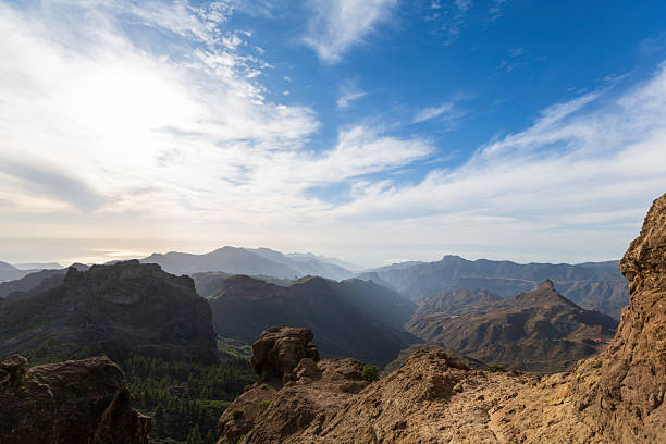 A vast mountain canyon panorama reveals jagged cliffs, deep valleys, and a luminous sky. Sunlight glints on rocky foregrounds while distant peaks fade into mist, offering a serene, expansive view of wilderness and adventure.