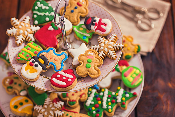 Stock photo showing close-up, elevated view of red and green plates of iced Christmas themed sugar cookies covered with royal icing, on a red background. Biscuits shaped like snowflakes and and baubles. Christmas food and home baking concept.