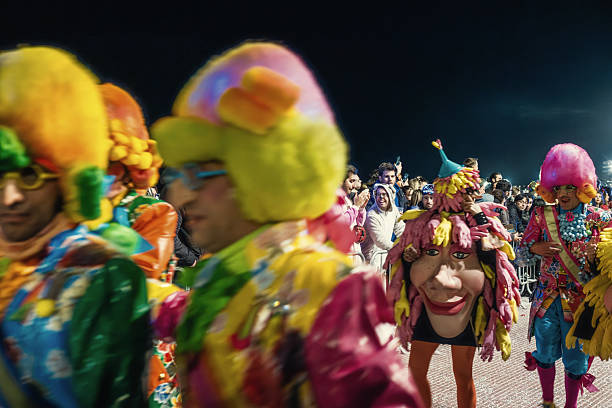 Sitges, Catalonia, Spain 02-27-2022: participants in vibrant costumes and elaborate wigs are celebrating during the Sitges carnival parade at night, with a crowd of spectators watching the festive event