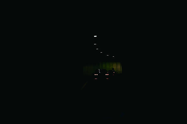 Car driving through a dark, long tunnel with brake lights visible