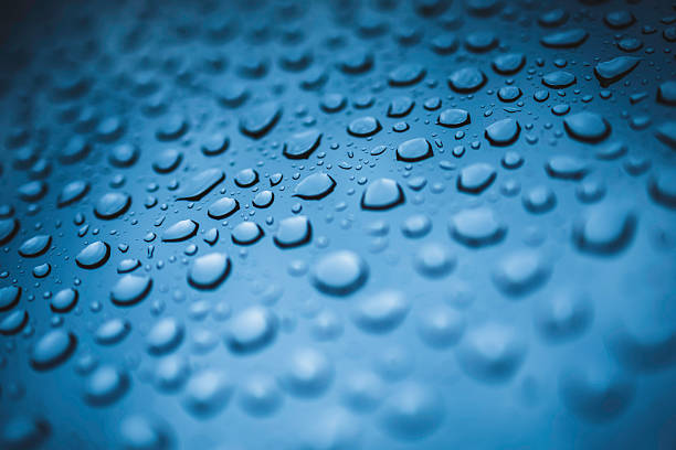 A vivid macro image featuring numerous water droplets clustered on a smooth blue surface. The droplets create a textured, reflective pattern that conveys freshness, moisture, and cool, serene aesthetics.