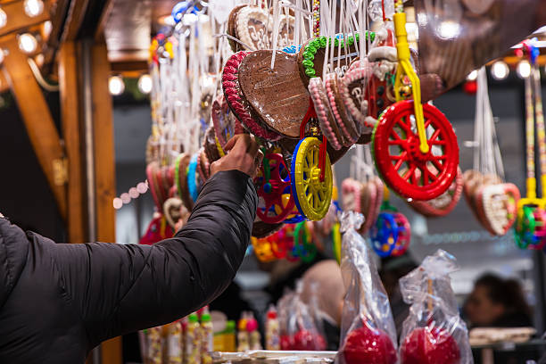 istock Customer's hand selecting an item at a vibrant display of colorful candy wheels, gingerbread hearts, and festive sweets at a traditional christmas market stall 2248443322