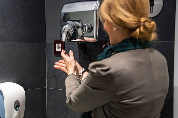 istock Woman using a hand dryer in a modern public restroom at midday 2248443522