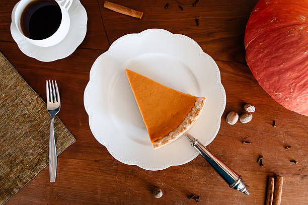 Slice of pumpkin pie being served on a white plate with coffee