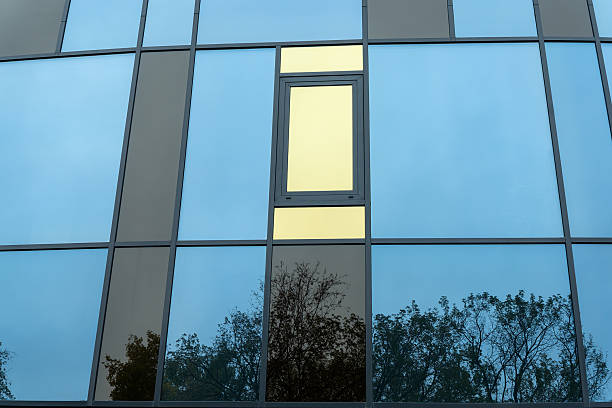 istock Modern building facade with blue and yellow glass windows in geometric grid pattern. Abstract urban architecture with reflective blue panels and asymmetric open windows on a contemporary glass facade. 2248451895