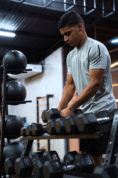 istock Hispanic man in gym selecting dumbbells from rack, concentrating on strength training and fitness. Achieving fitness goals 2248456603