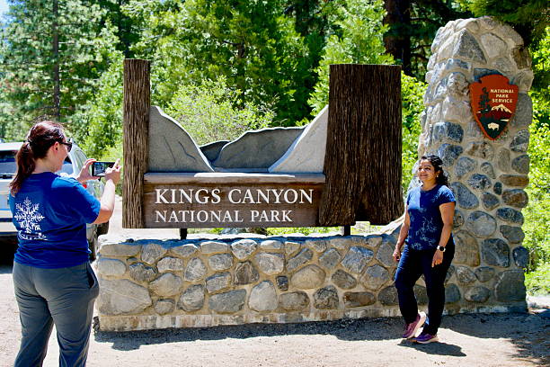 Northern California, USA - May 25, 2025: A woman takes a photograph of another woman visiting Kings Canyon National Park in front of an entrance sign to the public park.