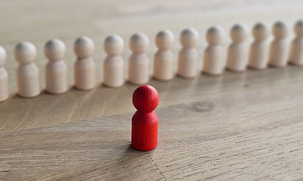 istock Group of wooden figures with a single red figure in front on a wooden surface representing individuality and leadership concept 2248469057