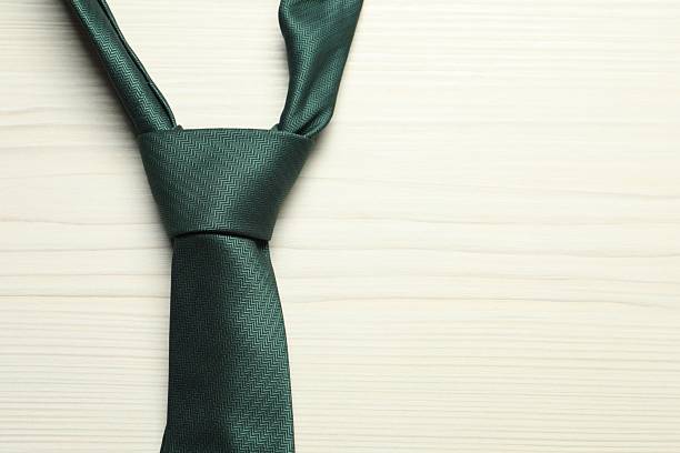 One green necktie on white wooden table, top view. Space for text