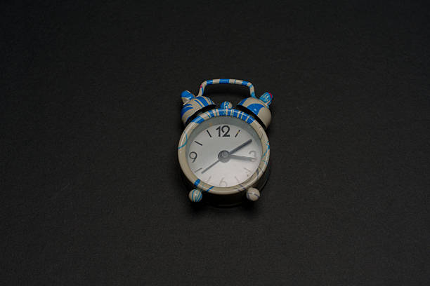 A colorful alarm clock with blue stripes and a round face rests on a dark surface. The clock features distinct hour markers and a simple design that draws attention.