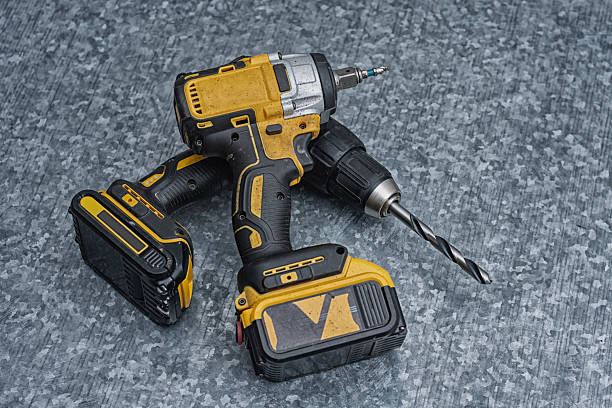 istock Two electric power tools, a yellow and black cordless drill and an impact driver, are resting on a gritty, textured grey galvanized metal or concrete background. 2248472960