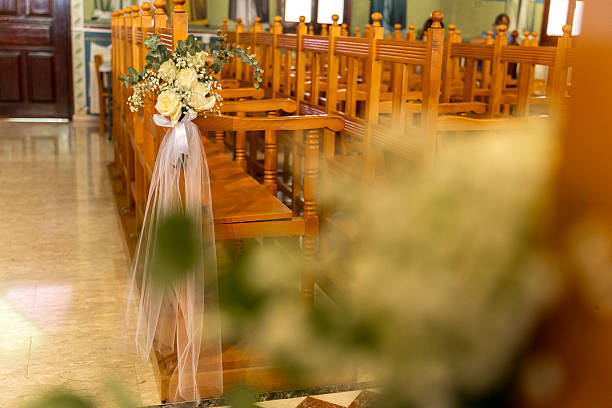 The delicate flower bouquets hardly stand out in the grayscale, but emphasize the elegance of the connectedness. In front of the dark background of the altar, framed by a cross and candles, these two chairs stand as a silent promise, as a pure canvas for the love that will soon begin. It is a scene of dignity and expectation that reminds us of the fundamental, unshakable contrasts from which a life together is woven.