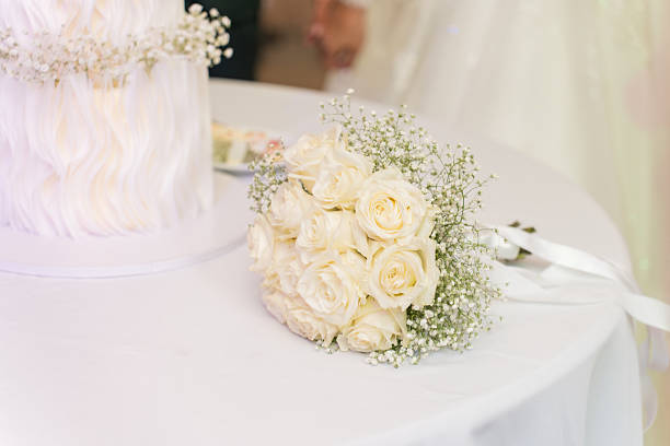 A stunning arrangement of white roses and baby's breath is displayed on a table at a wedding reception. Soft lighting enhances the romantic atmosphere of the event.