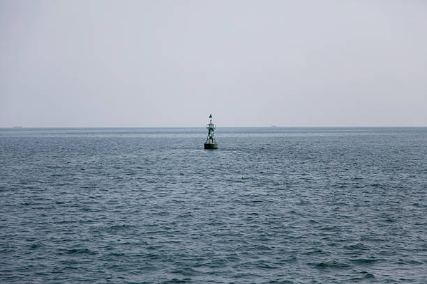 A single buoy floating on the calm surface of a large expanse of water under a grey sky.