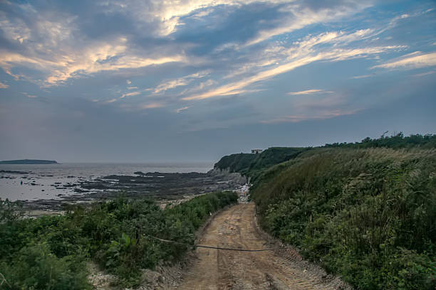 A scenic coastal path surrounded by lush vegetation under a dramatic sky with a view of the sea.