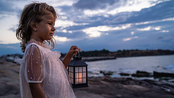 istock Child with Lantern by Shore at Dusk, Soft Light Embracing Nature and Innocence. 2248487818