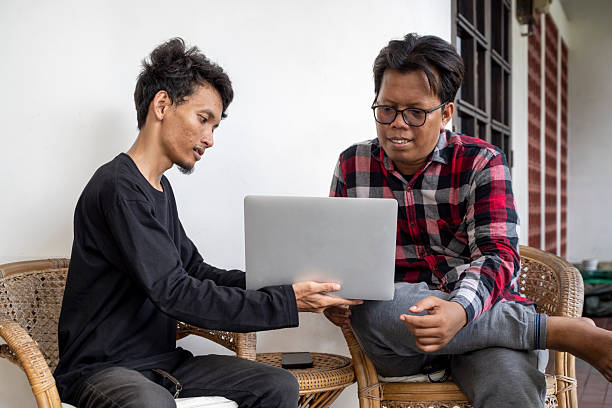 Two Indonesian southeast asian men are having a discussion. Holding a laptop while sitting at home. Work from home