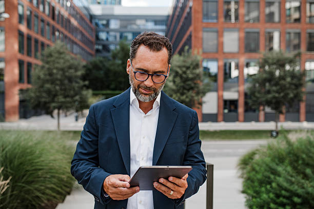 istock Businessman in front of office building, holding tablet and reading something. 2248489918