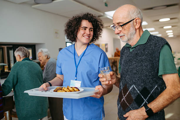 istock Senior man having lunch with supportive caregiver in community center cafeteria. 2248490088