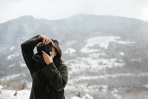 Woman taking a picture in a snowy environment with a vintage camera. She wears winter clothes and a hat.
