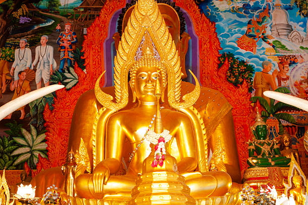 Golden thai buddha statue framed by gold ornate element in yard of Wat Phra Doi Suthep in Chiang Mai city. Located in outskirts on mountain and built in 19th century. From both side elephant teeth are reaching as bow in front of statue into the place