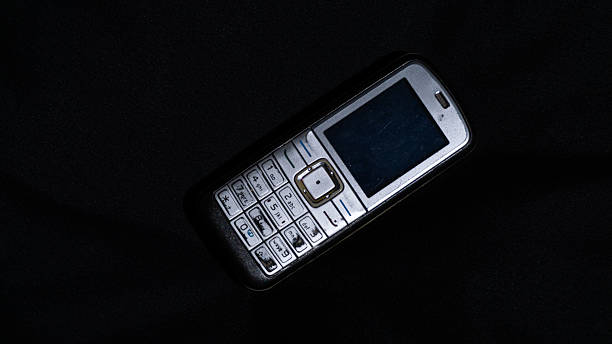 A classic feature phone photographed on black fabric with dramatic lighting, showing its scratched keypad and retro layout. Suitable for themes of old devices and digital history.
