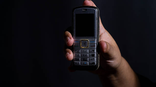istock Front view of a vintage mobile phone held in a hand against a dark studio background, showcasing its keypad and small screen. Ideal for illustrating obsolete tech or messaging 2248493371