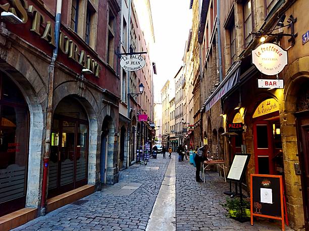 February 24. 2020. Lyon. France. A narrow, atmospheric cobblestone street in Vieux Lyon, lined with traditional restaurants and trattorias housed in old buildings with deep arched doorways.