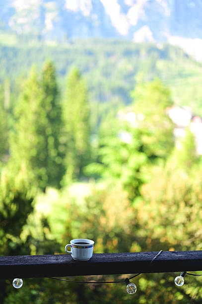 Coffee cup resting on a wooden balcony railing with a blurred green mountain landscape