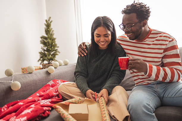 istock Diverse couple wrapping christmas gifts together on sofa 2248503439