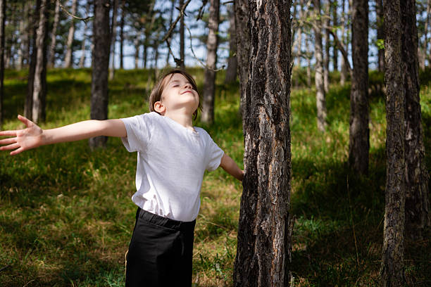 Young child with closed eyes and outstretched arms breathing fresh air and feeling sunlight in a peaceful forest setting
