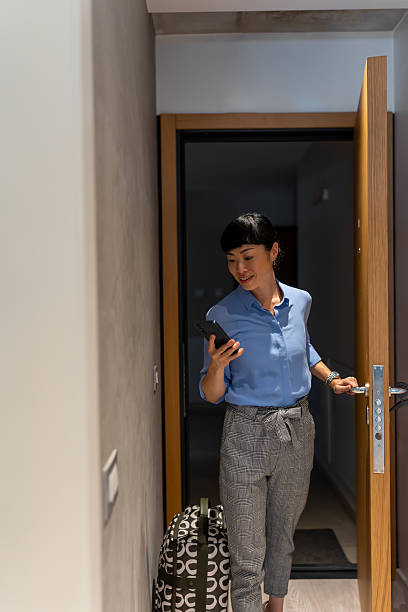 istock Asian businesswoman arriving in a modern guest room, checking her phone while pulling a suitcase 2248511071