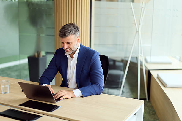 istock Professional Man in Blue Suit Working on Laptop at Modern Office Desk in Bright Workspace 2248517160
